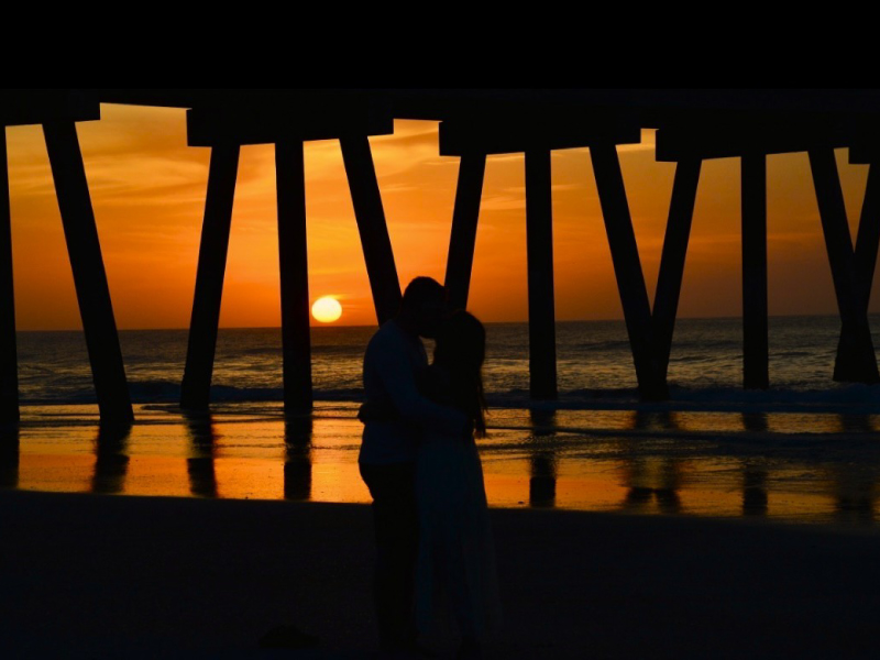 Couple under pier at sunset