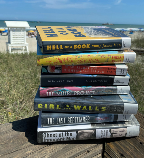 stack of books at the beach, published by UNCW alumni authors