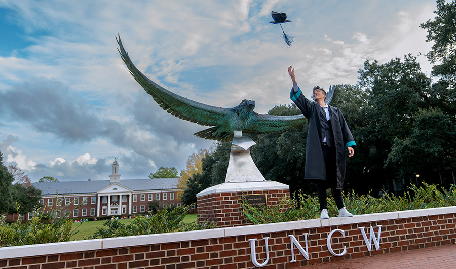 Grad throwing cap in front of Seahawk statue on Hoggard Lawn