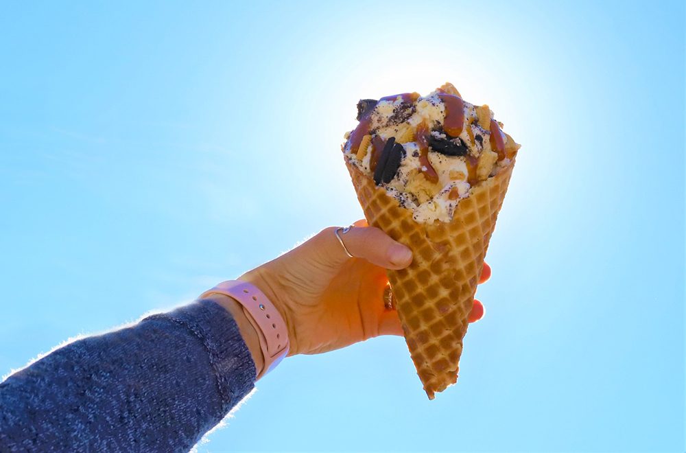 A photo of an overflowing ice cream cone being held in front of the sun.