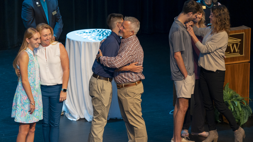 A group of UNCW alumni stand on stage with current students during the Legacy Pinning Ceremony.