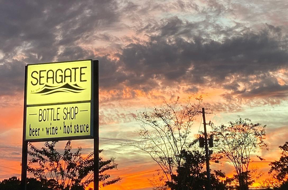A photo of Seagate Bottle Shop's sign as the sun is setting and turning the sky orange.